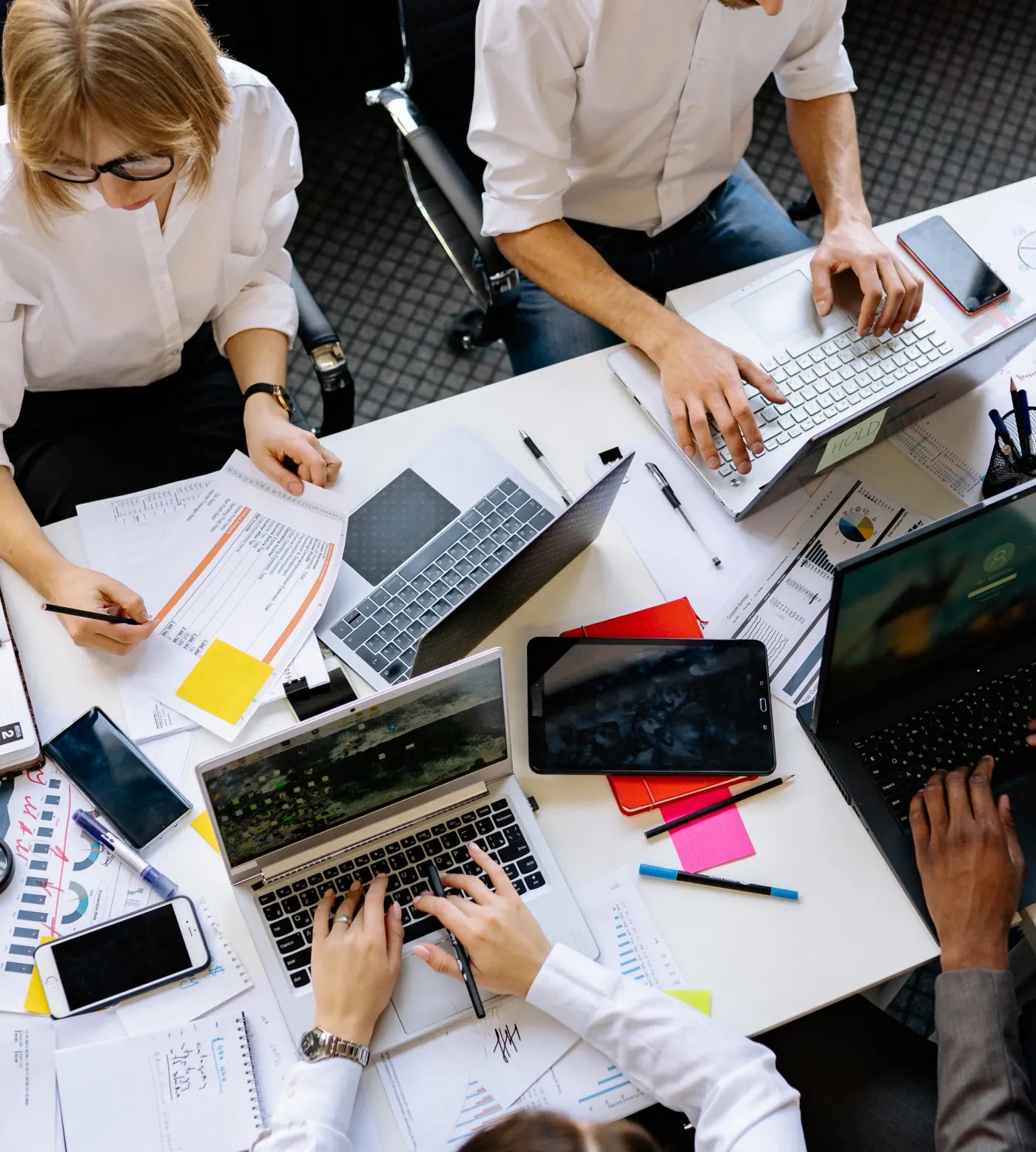 Overhead view of a team working across laptops, notes and charts