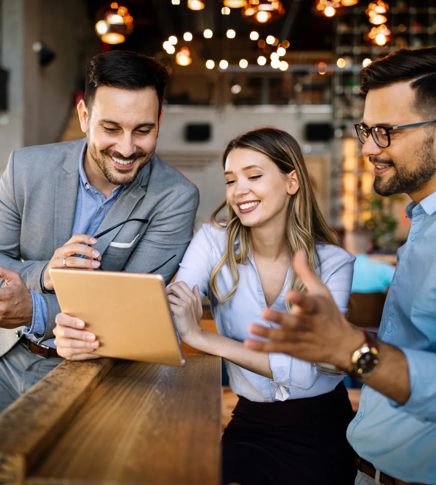 Three colleagues smiling over a tablet in a warmly lit cafe